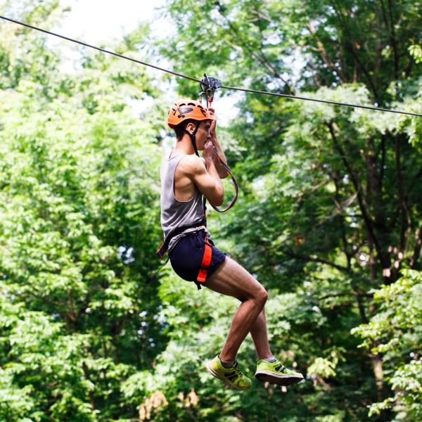 A man enjoying a fun zip-line ride high above the trees, smiling as he flies through the green forest.