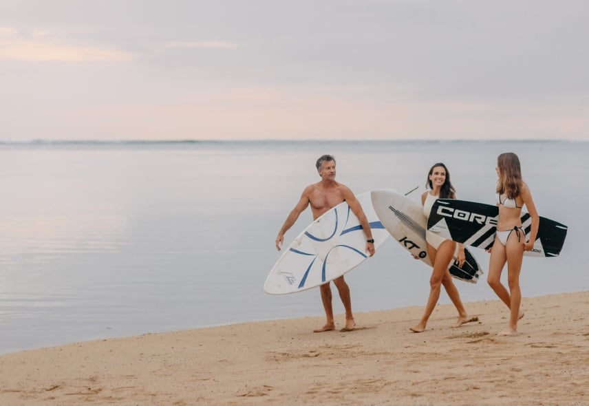 Family walking along the beach carrying a surfboard