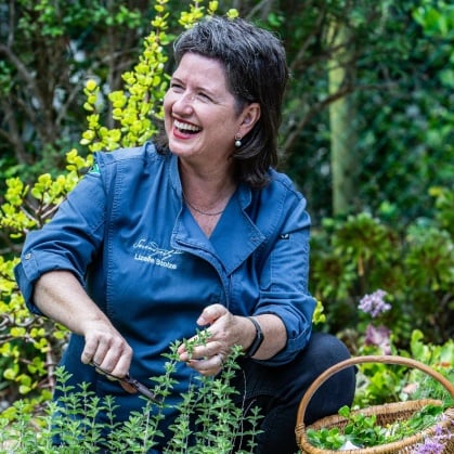 chef Lizelle Stolze pflückt frischen thymian im garten mit strahlendem lächeln