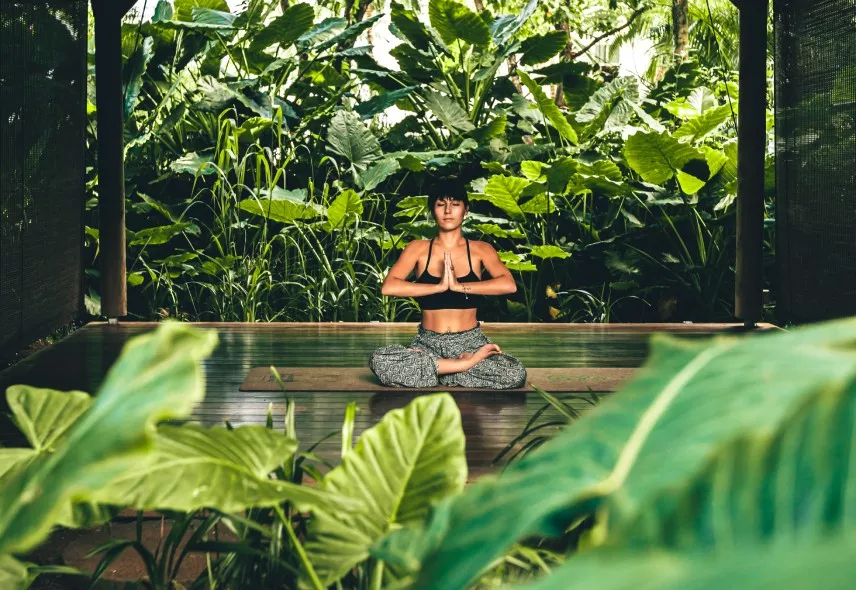 Woman meditating in nature surrounded by lush greenery, embracing mindfulness and inner peace