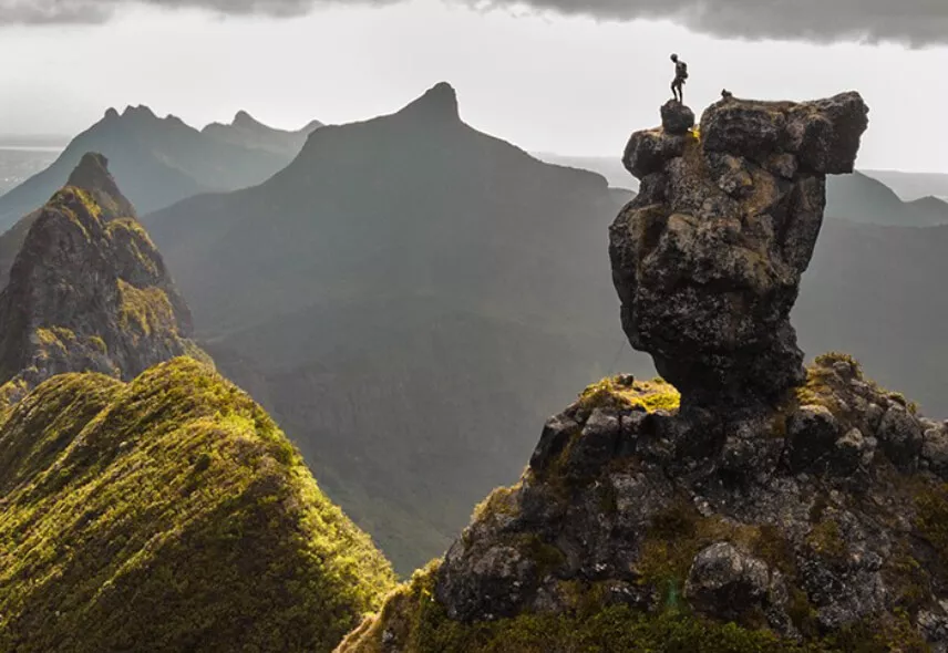 Hiker standing triumphantly on the summit of Pieter Both Mountain in Mauritius, overlooking scenic landscapes