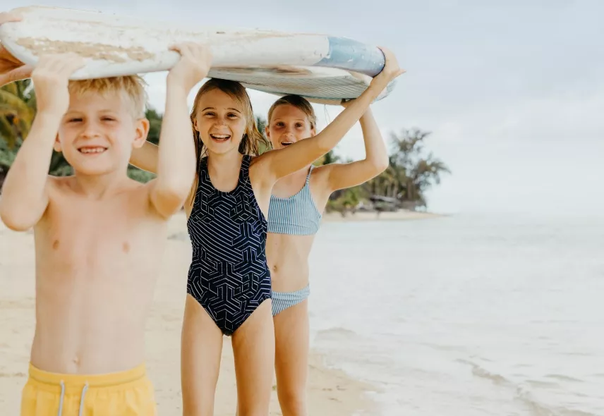 Children holding a surfboard on a sunny beach day